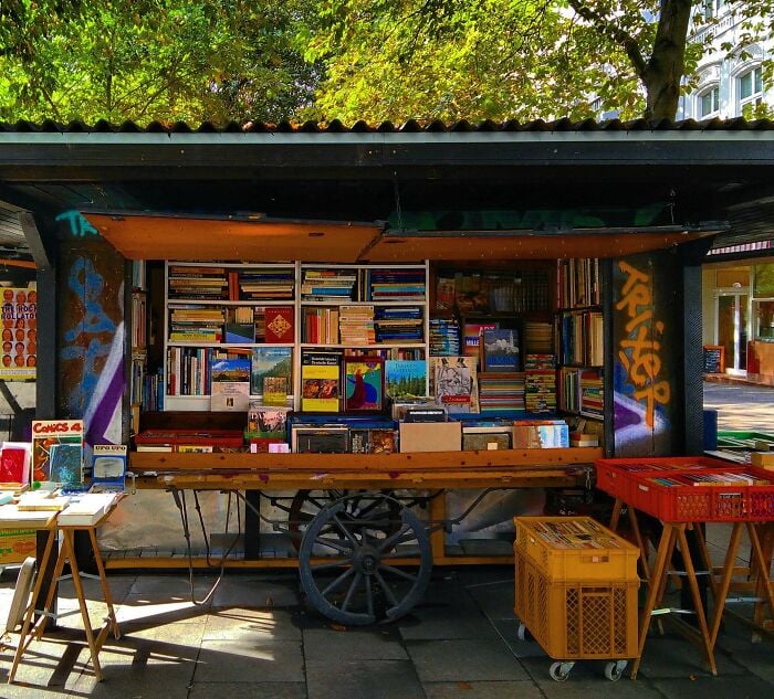 Livraria aconchegante ao ar livre com prateleiras cheias de livros, cercada por vegetação, exibindo bibliotecas e livrarias mágicas. Livraria aconchegante ao ar livre com prateleiras cheias de livros, cercada por vegetação, exibindo bibliotecas e livrarias mágicas.