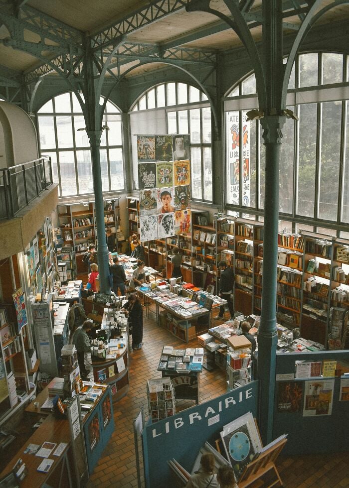 Spacious, grandiose library with high arched windows, tall metal columns, and shelves filled with books and visitors browsing. Spacious, grandiose library with high arched windows, tall metal columns, and shelves filled with books and visitors browsing.