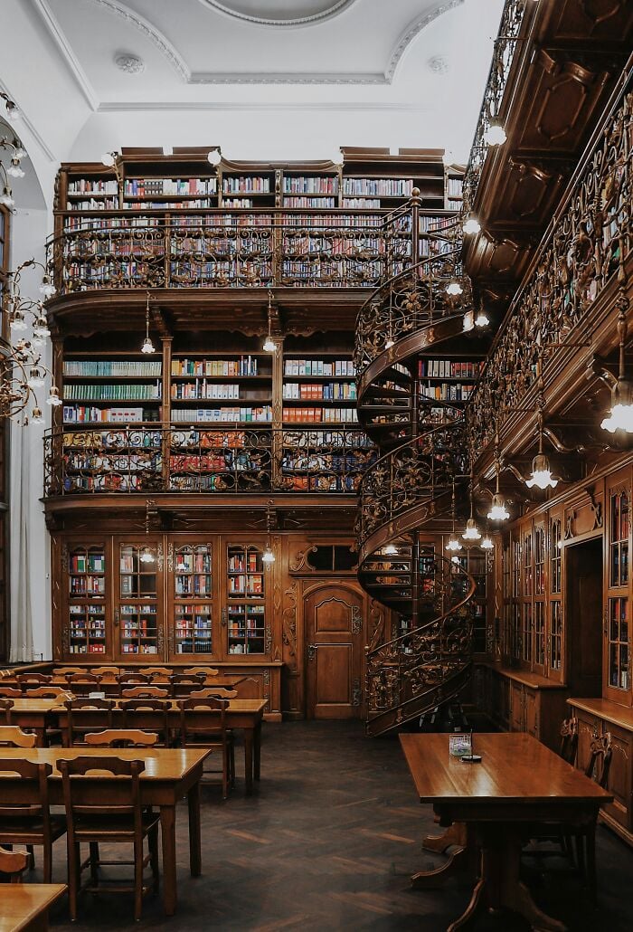 Grandiose Bibliothekseinrichtung mit Holzregalen, Wendeltreppe und gemütlichen Lesetischen voller Bücher aus aller Welt.