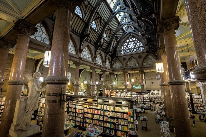 Interno grandioso di biblioteca con colonne imponenti, soffitti a volta e scaffali pieni di libri in un'ambientazione magica. Interno grandioso di biblioteca con colonne imponenti, soffitti a volta e scaffali pieni di libri in un'ambientazione magica.