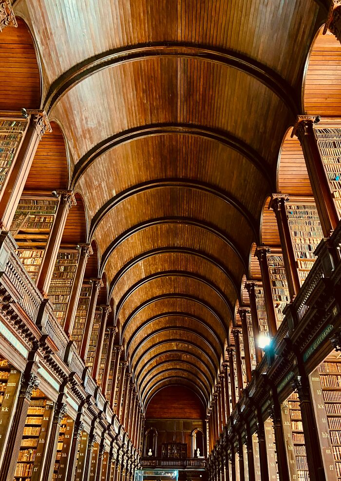 Grandiose library interior with high wooden vaulted ceiling and tall bookshelves filled with books from floor to ceiling. Grandiose library interior with high wooden vaulted ceiling and tall bookshelves filled with books from floor to ceiling.